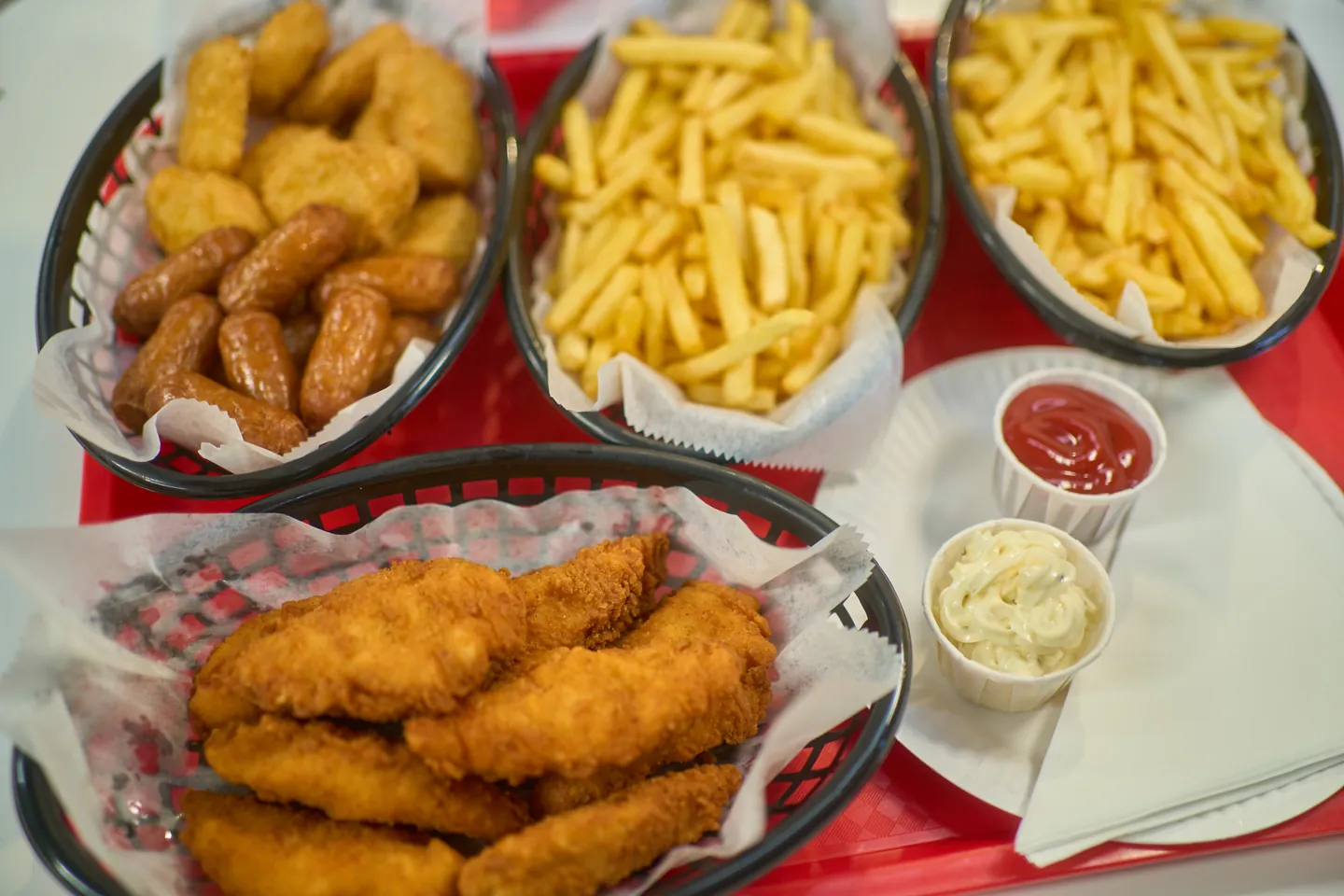 A family sharing tray with chicken goujons, nuggets, cocktail sausages, fries and two dips