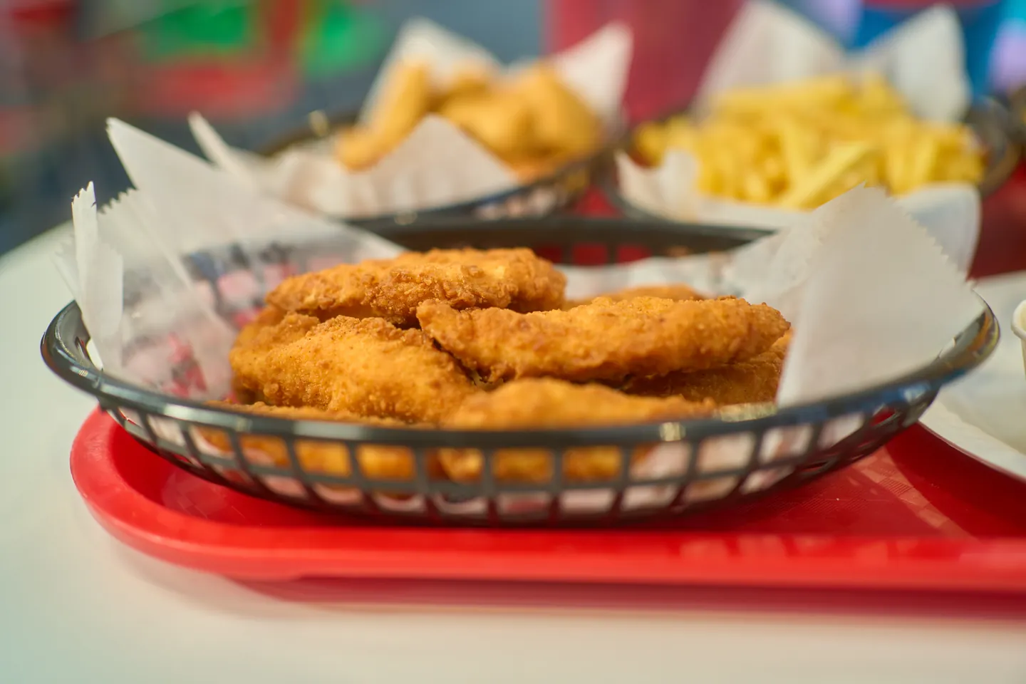 Golden battered chicken goujons in a lined basket, with other baskets softly out of focus behind