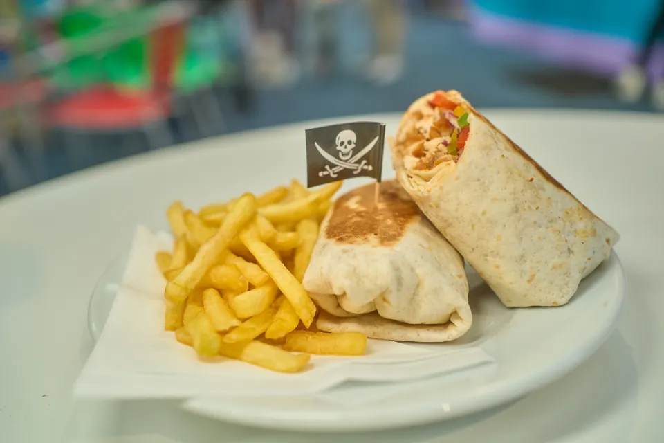 A wrap cut in half on a plate beside fries at Pirates Adventure café